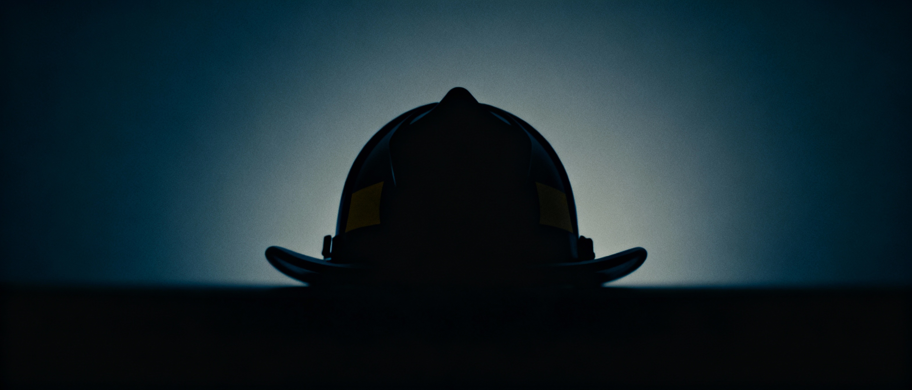 Mourning firefighter silhouette with a helmet against a deep blue gray gradient